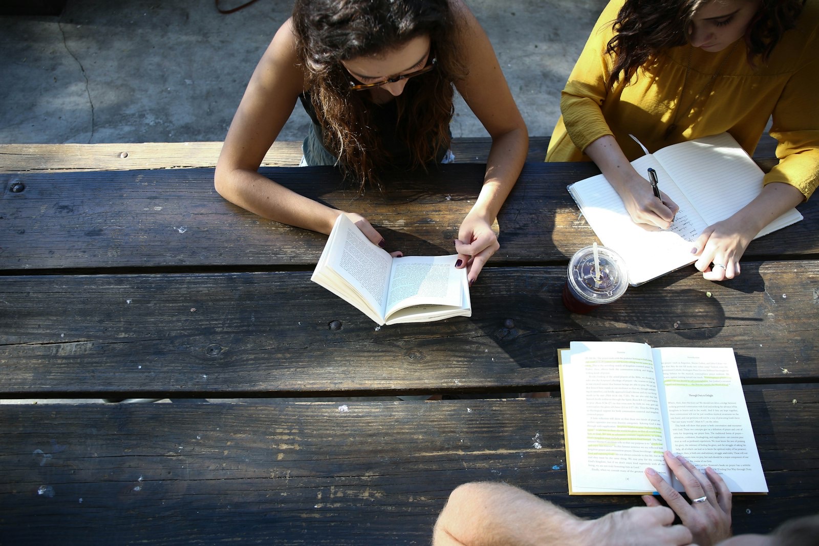 Two students reading and writing notes at a picnic table.